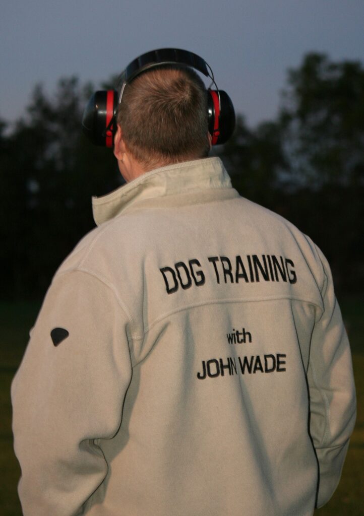 Photo of John Wade during a training session at night. He has his back turned to the camera and is wearing a jacket with "Dog training with John Wade" embroidered. 